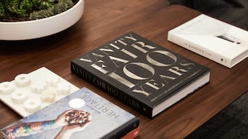 Una mesa de madera con una planta en maceta, un libro titulado 'Vanity Fair 100 Years' y otro libro titulado 'The Kinfolk Home'.