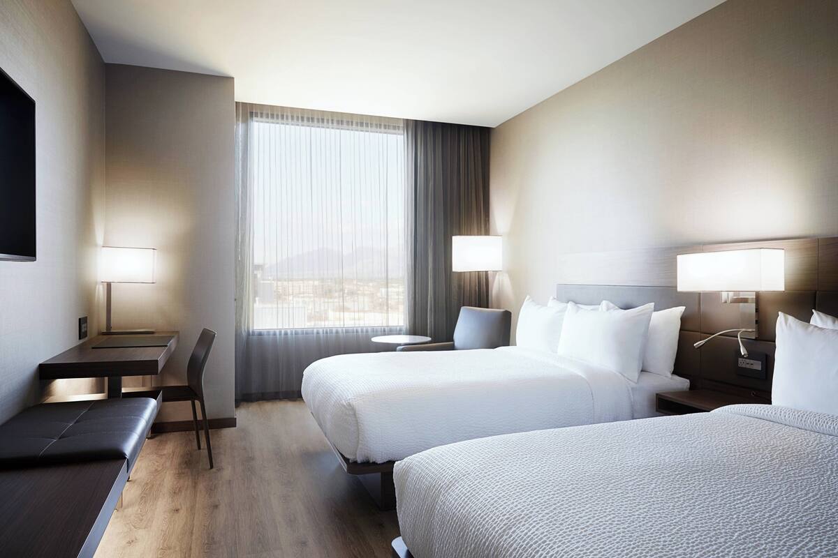 A hotel room with two beds, a desk, a chair, and a small table.