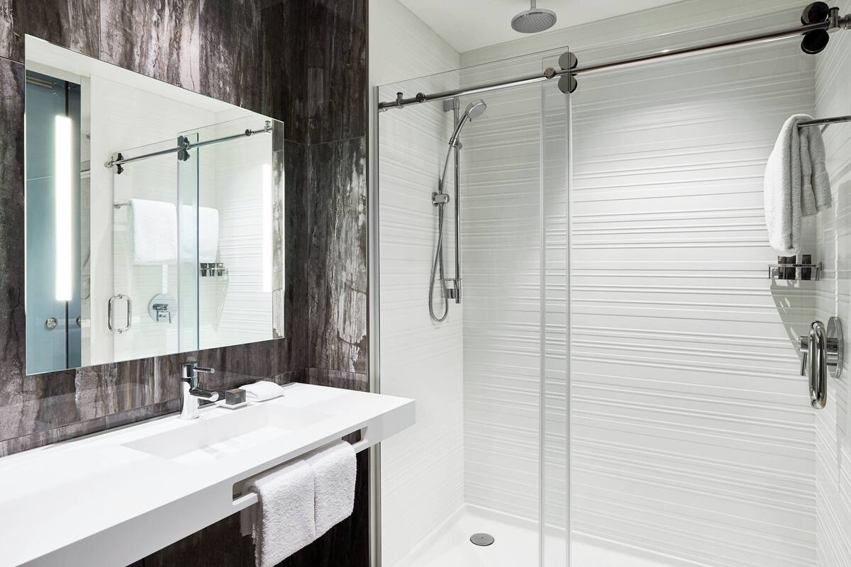 A modern bathroom with a glass shower enclosure, a white sink with a mirror, and a towel rack.