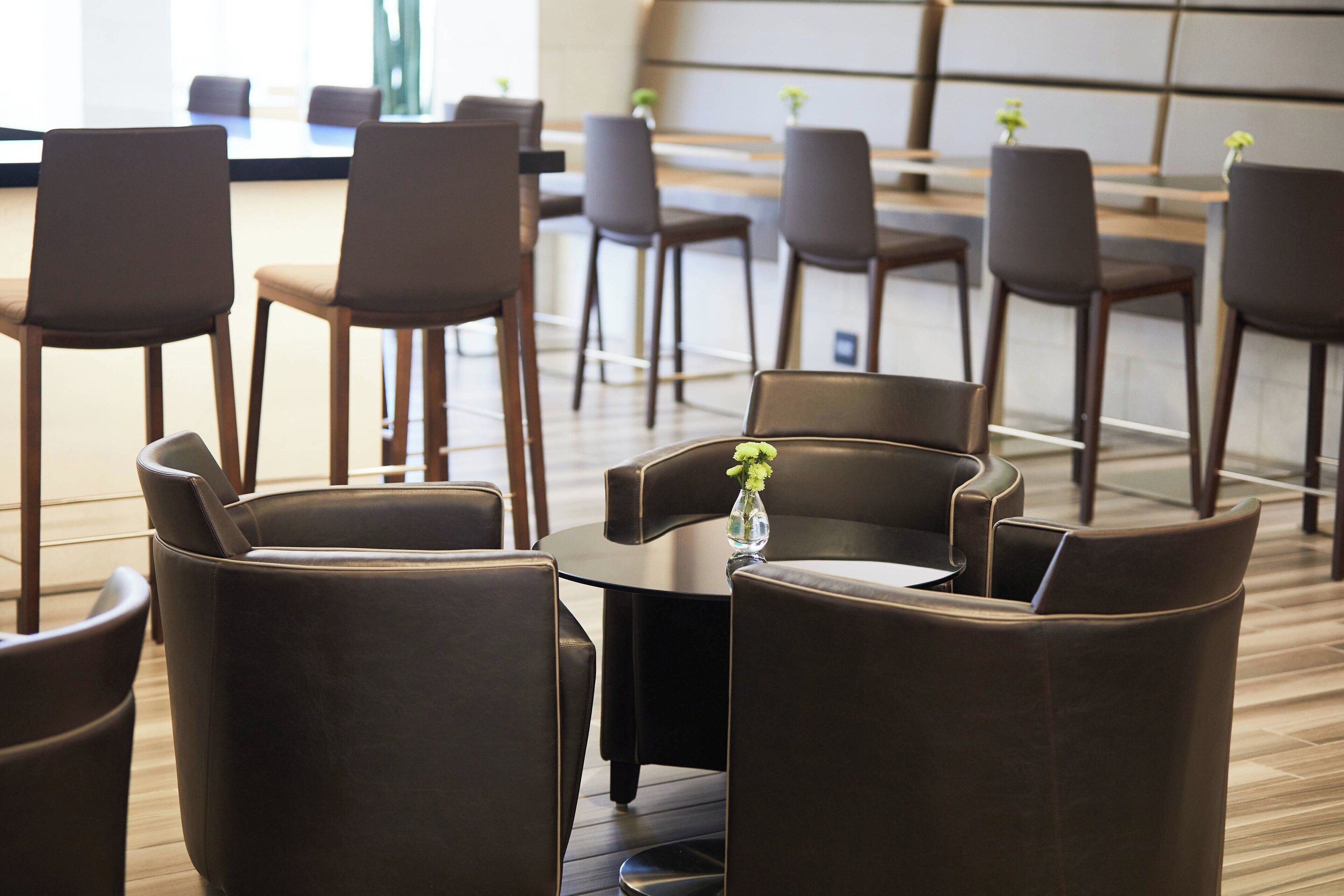 A modern hotel lobby with leather chairs and a round table, featuring a vase with flowers.
