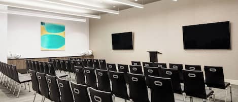 A conference room with rows of black chairs, a large screen, and a projector on the wall.