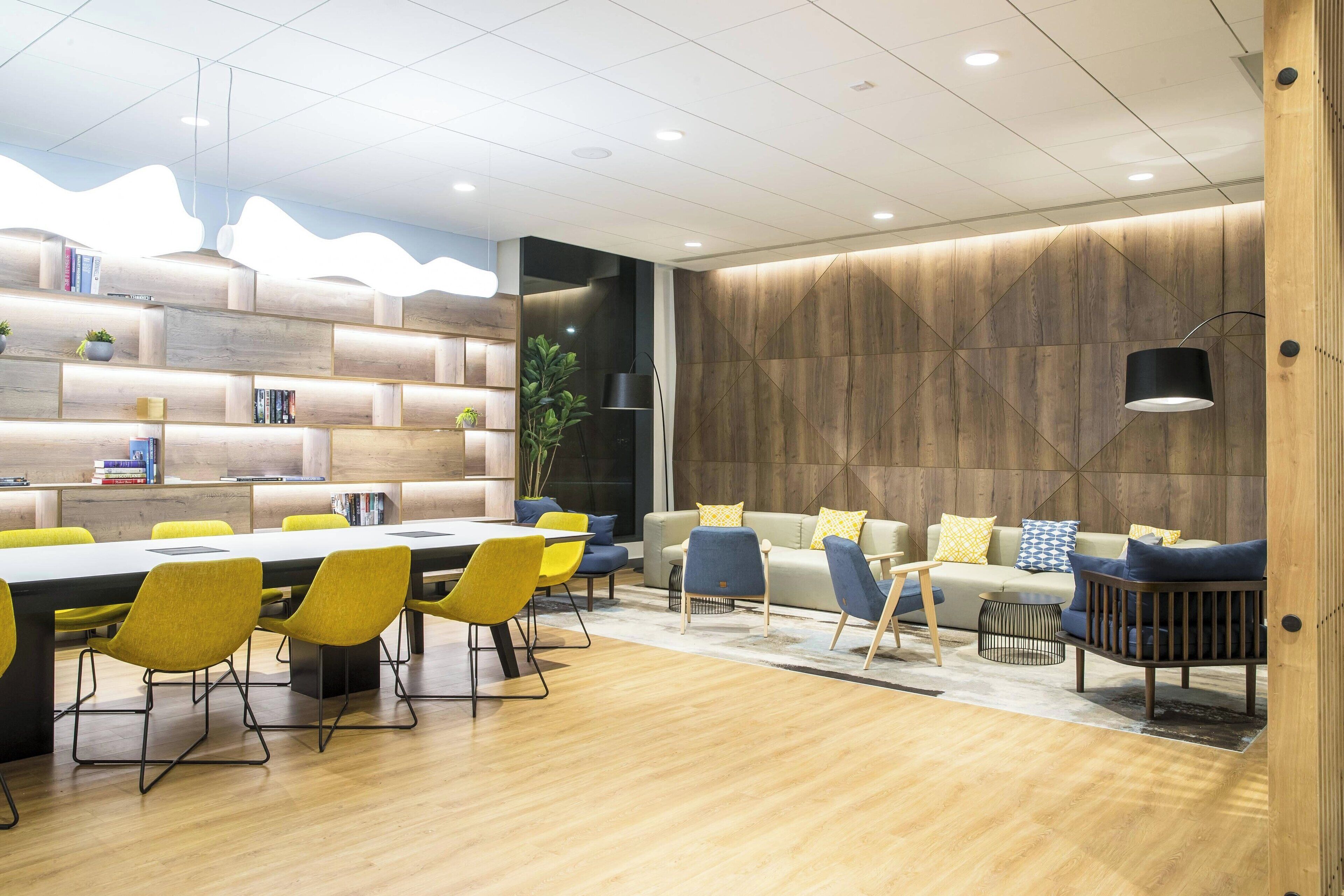 Una sala de reuniones moderna con una mesa larga, sillas amarillas y un sofá con cojines azules y amarillos.
