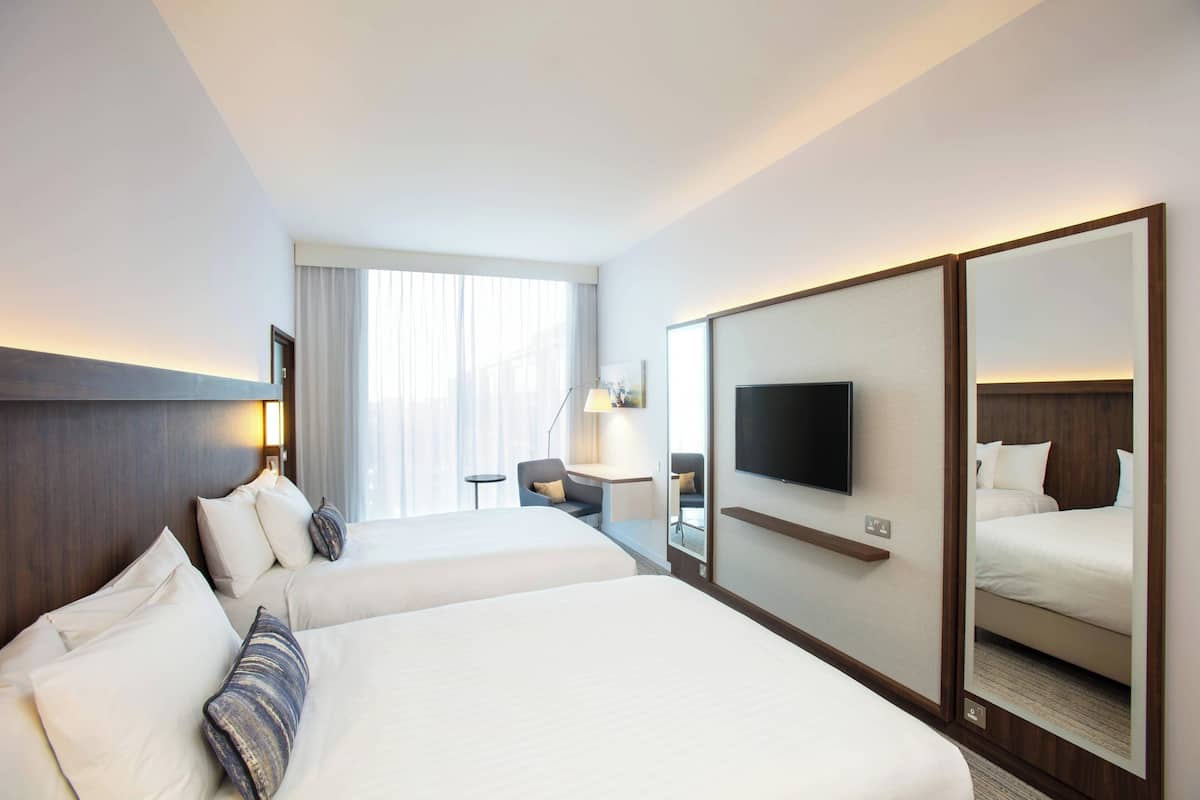 A hotel room with two beds, a desk, a chair, a TV, and a large mirror.
