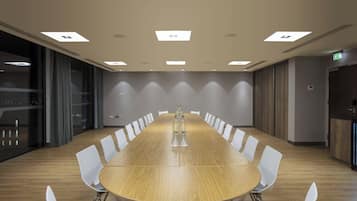 Un salón de conferencias con una larga mesa de madera, sillas blancas e iluminación empotrada en el techo.
