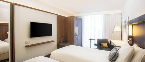 A hotel room with two beds, a TV mounted on the wall, a desk, and a chair.