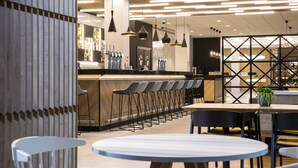 A modern bar area with a long counter, multiple bar stools, and pendant lighting. - Courtyard by Marriott Edinburgh West (Edinburgh)
