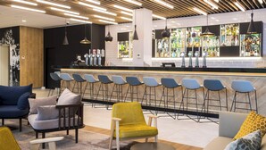 A modern bar area with a long counter, multiple bar stools, and hanging pendant lights. - Courtyard by Marriott Edinburgh West (Edinburgh)