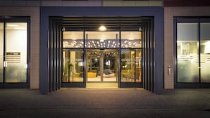 A modern hotel entrance with glass doors, a well-lit interior, and a visible seating area outside. - Courtyard by Marriott Edinburgh West (Edinburgh)