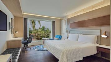 Ein Hotelzimmer mit einem großen Bett, einem Schreibtisch, einem Stuhl und Blick auf Palmen.