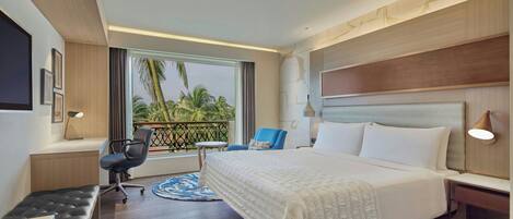 A hotel room with a large bed, a desk, a chair, and a view of palm trees.
