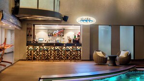Eine Poolbar mit Neonreklame, einer Theke und einer Sitzecke mit Korbstühlen.