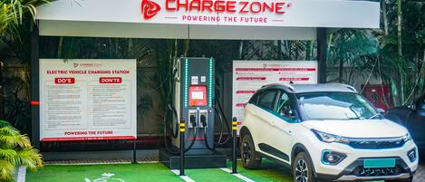An electric vehicle charging station with a white SUV parked, surrounded by greenery and palm trees.