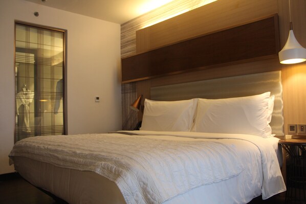 A hotel room with a large bed, a wooden headboard, a bedside table with a lamp, and a sliding glass door.