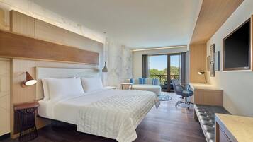 A modern hotel room with a large bed, a desk, a chair, and a sofa.
