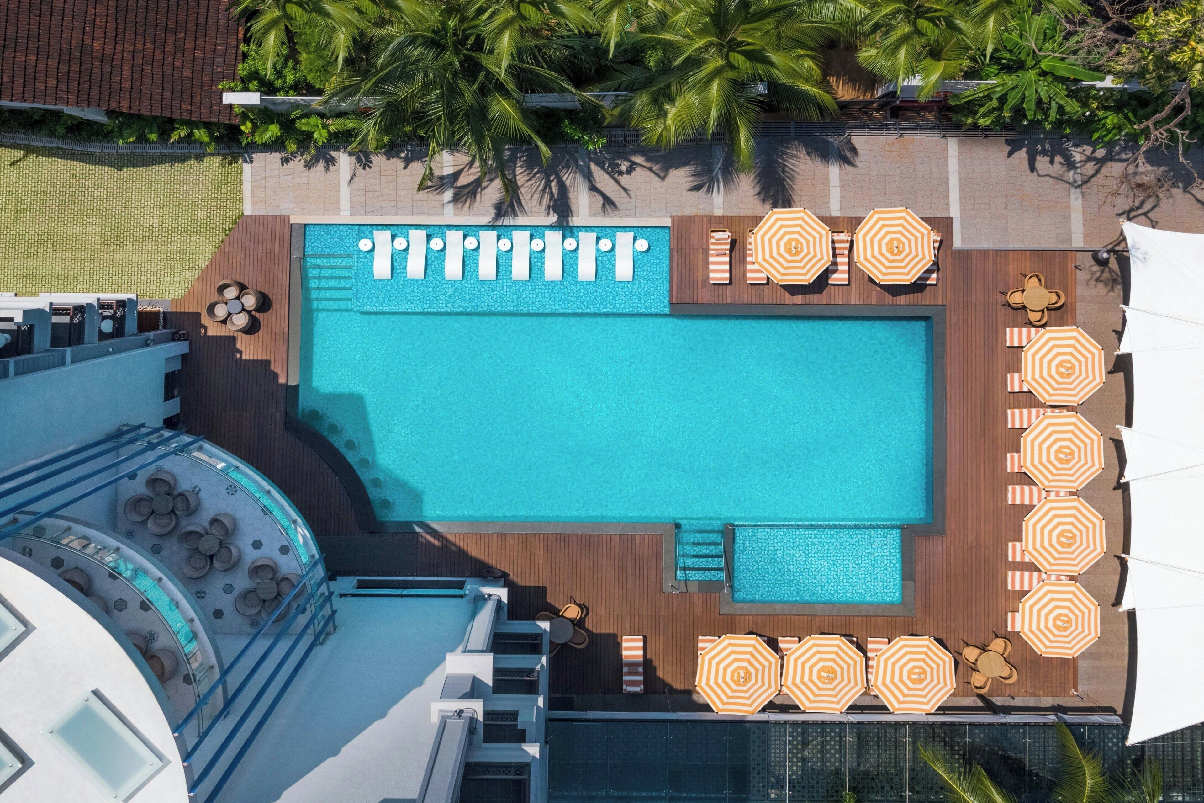 Vue aérienne d’un espace piscine sur le toit, comprenant plusieurs piscines, des chaises longues et des parasols.