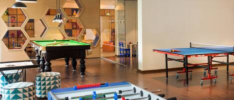 A room with a foosball table, a pool table, and a billiards table.
