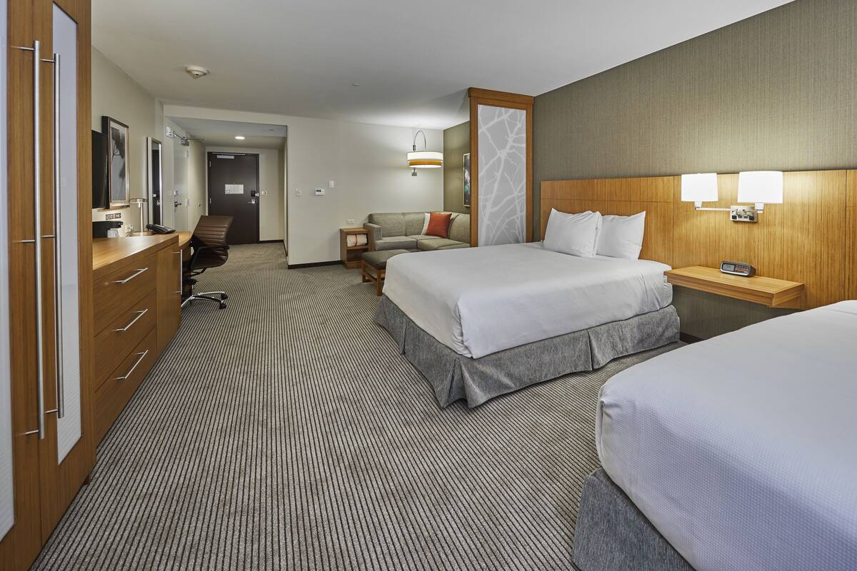 A hotel room with two beds, a desk, a chair, a wardrobe, and a bathroom visible through an open door.