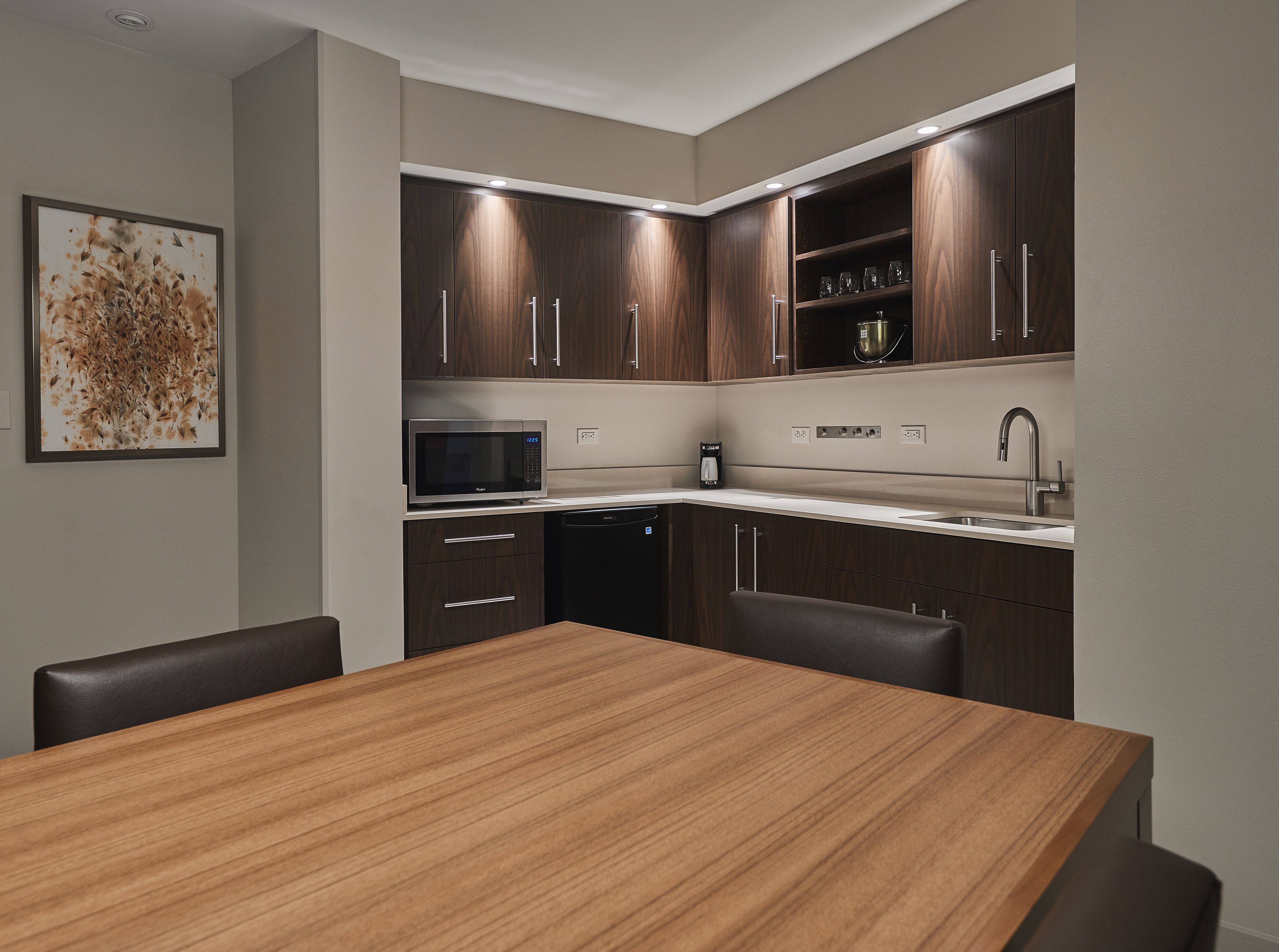 A modern kitchen with dark wood cabinets, a stainless steel microwave, a coffee maker, and a sink.