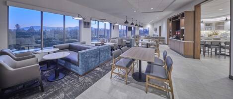 Un moderno vestíbulo de hotel con zonas de estar, ventanas amplias con vistas a la ciudad y un área de bar.