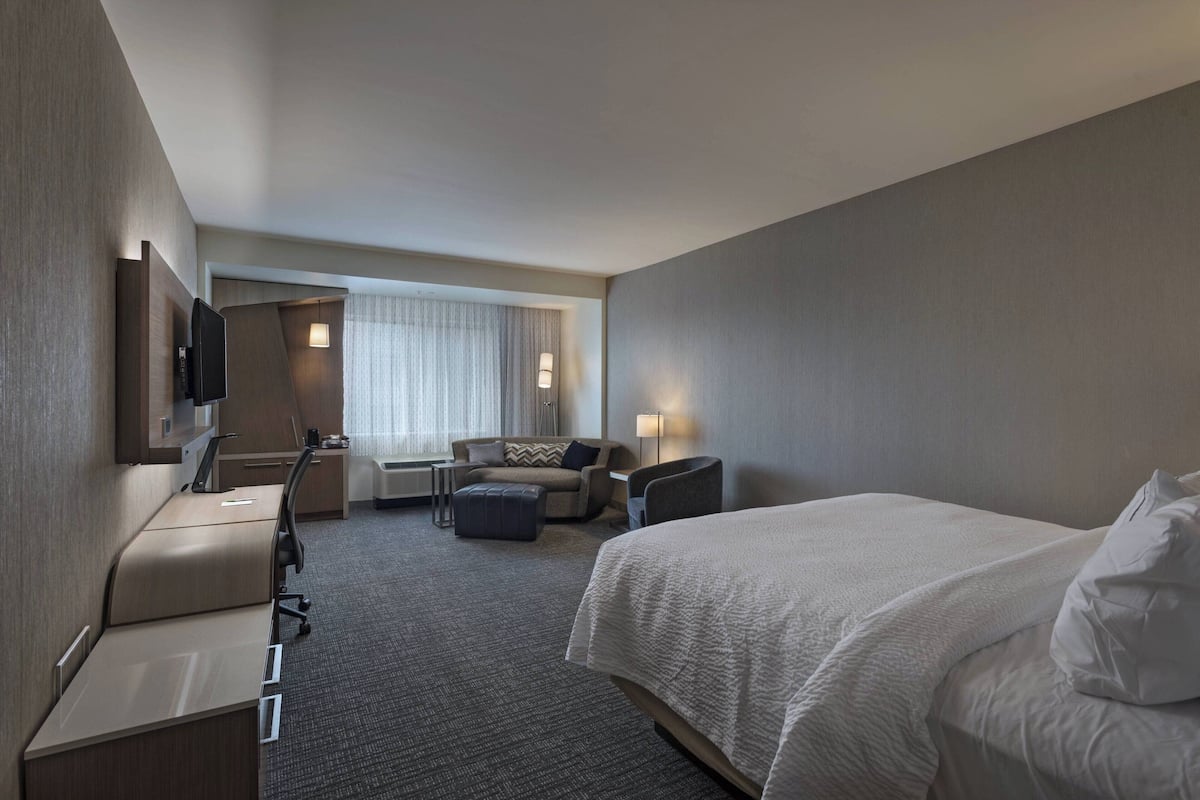 A hotel room with a bed, a desk, a chair, a sofa, and a TV.