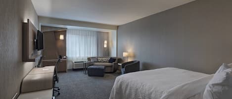 Una habitación de hotel con cama, escritorio, sillón, sofá y televisor.