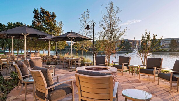 An outdoor patio with seating and umbrellas overlooking a body of water. - Courtyard by Marriott Houston Sugar Land/Lake Pointe (Sugar Land)
