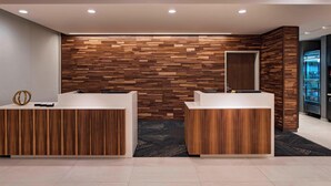 A reception area with two wooden reception desks, a patterned wall, and a refrigerator in the background. - Courtyard by Marriott Houston Sugar Land/Lake Pointe (Sugar Land)
