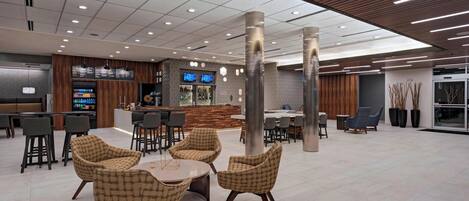 A modern indoor space with seating areas, a bar, and a counter with digital displays.