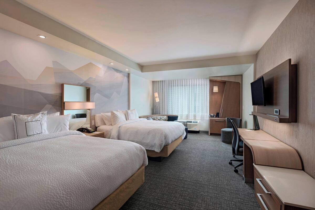 A hotel room with two beds, a desk, a chair, a TV, and a bathroom.