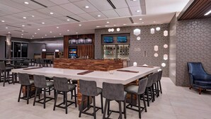 A modern bar area with a long counter, multiple seating options, and a bar stocked with various bottles. - Courtyard by Marriott Houston Sugar Land/Lake Pointe (Sugar Land)