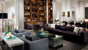 Een moderne woonkamer met een donkerbank, fauteuils, een salontafel en een boekenplank vol decoratieve objecten.