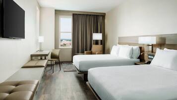 Habitación de hotel con dos camas, un escritorio, una silla y un televisor.