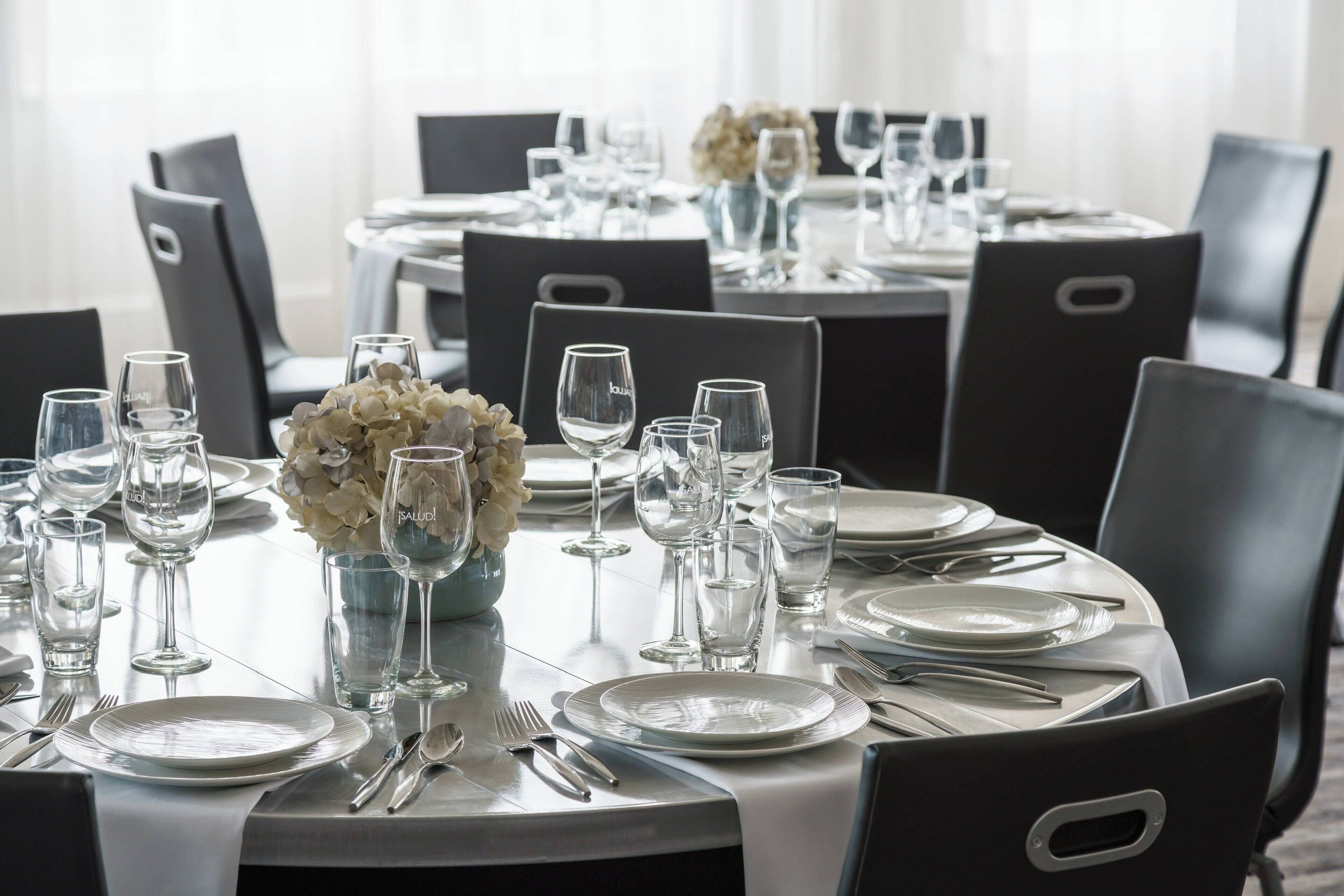 A dining table set with plates, cutlery, and wine glasses, surrounded by chairs.