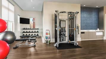 A modern gym with exercise equipment, a wall-mounted TV, and a variety of weights.