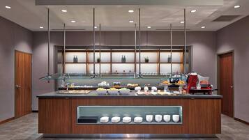 Un comptoir de petit-déjeuner moderne avec un plateau en verre, divers aliments et une machine à café.