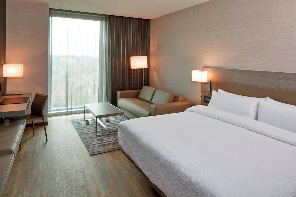 Una habitación de hotel con una cama grande, un sofá, un escritorio y una ventana con cortinas.