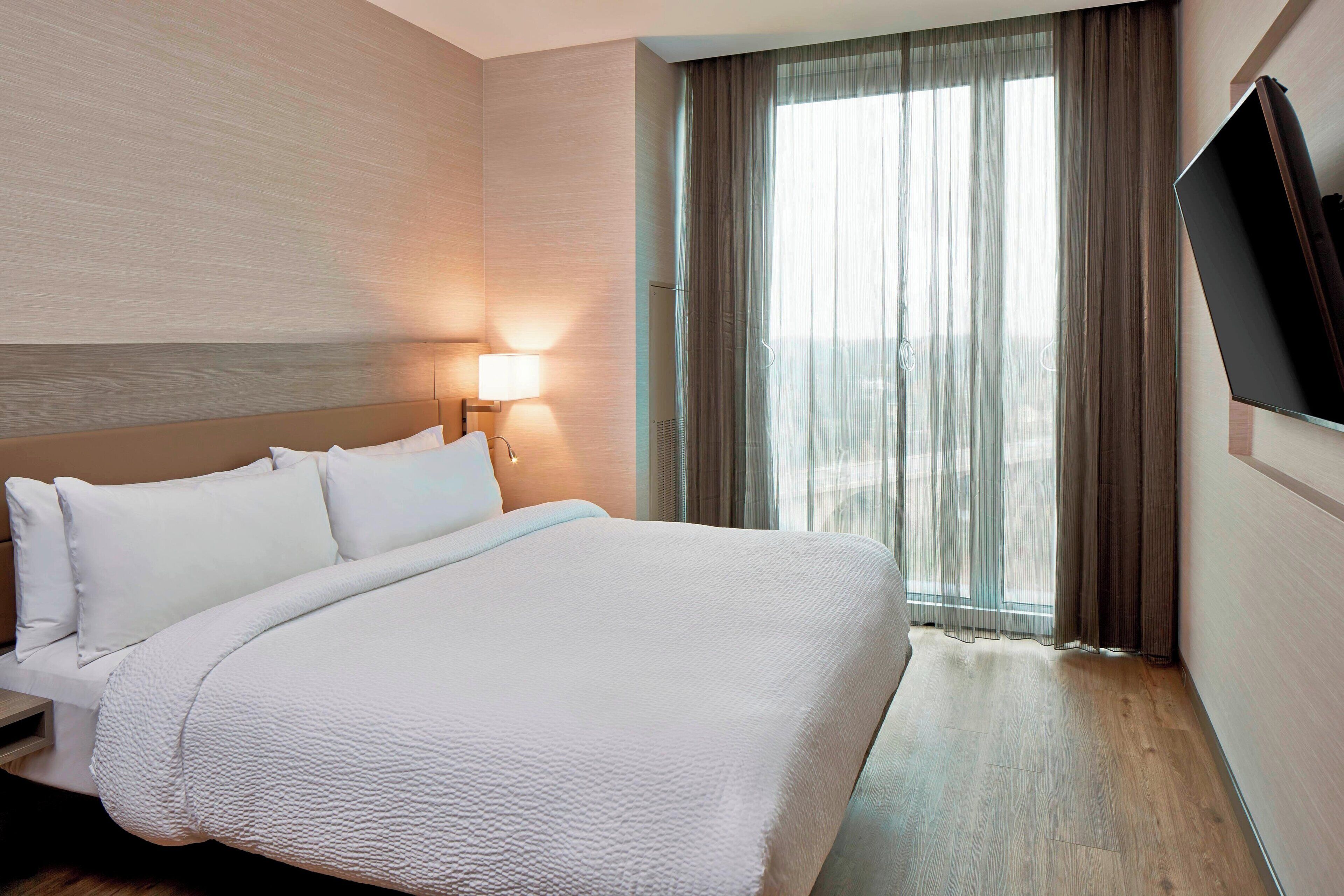 Una habitación de hotel con una cama grande, una mesita de noche, una lámpara y un televisor montado en la pared.