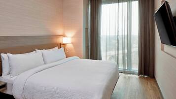 Una habitación de hotel con una cama grande, una mesita de noche, una lámpara y un televisor montado en la pared.