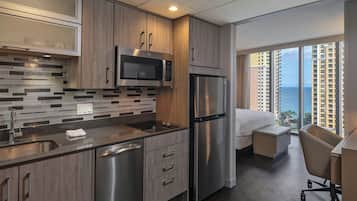 A modern kitchen with stainless steel appliances, a large window with a view of high-rise buildings, and a small seating area with a desk and chair.