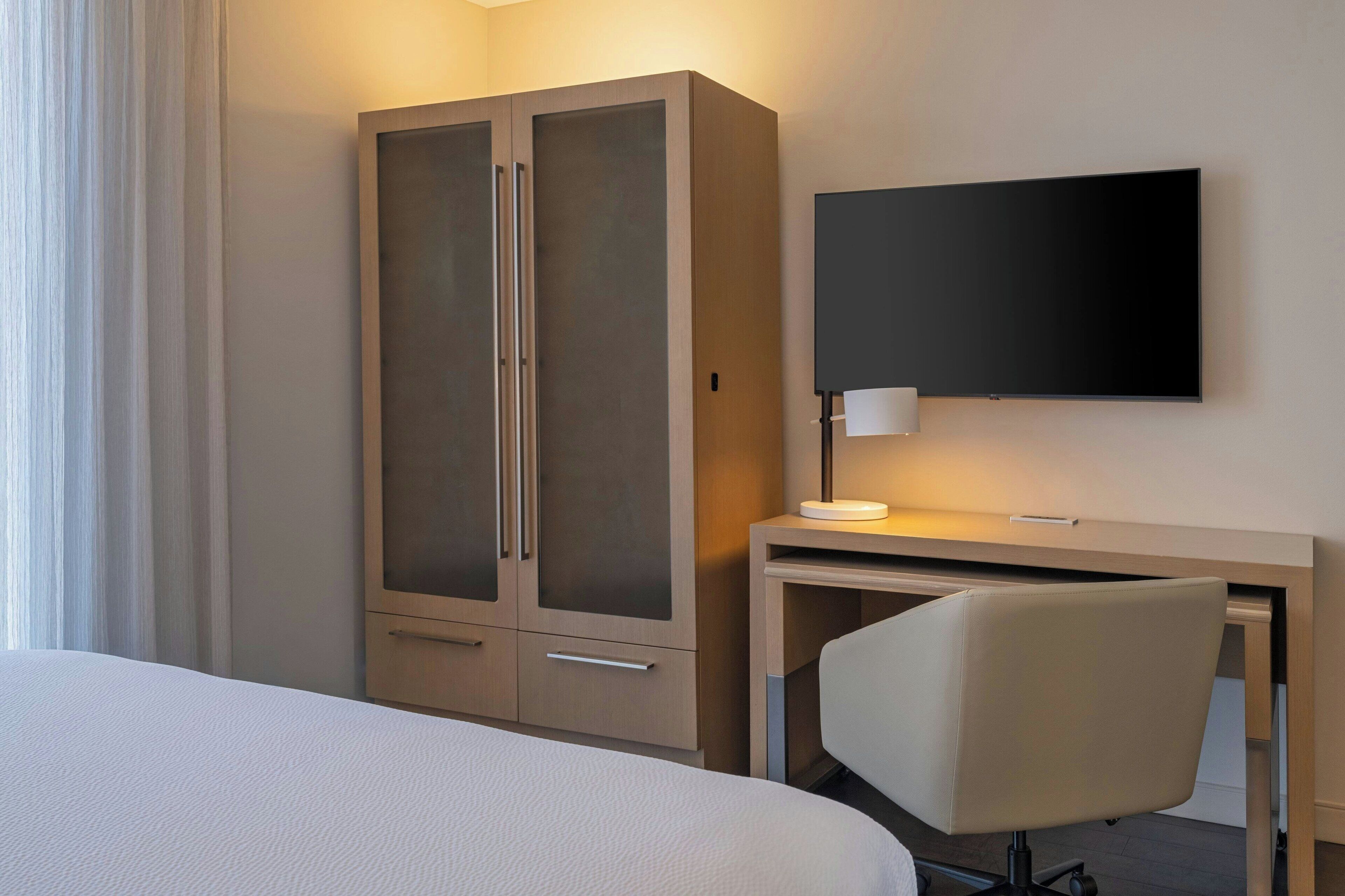 A hotel room with a bed, a desk with a chair, a television, and a wardrobe.