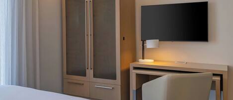 A hotel room with a bed, a desk with a chair, a television, and a wardrobe.