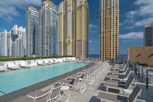 Zona de piscina en la azotea con sillones y vistas a edificios altos.