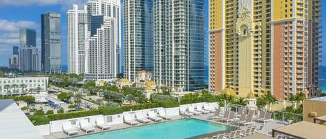 A rooftop pool area with lounge chairs and a view of high-rise buildings.
