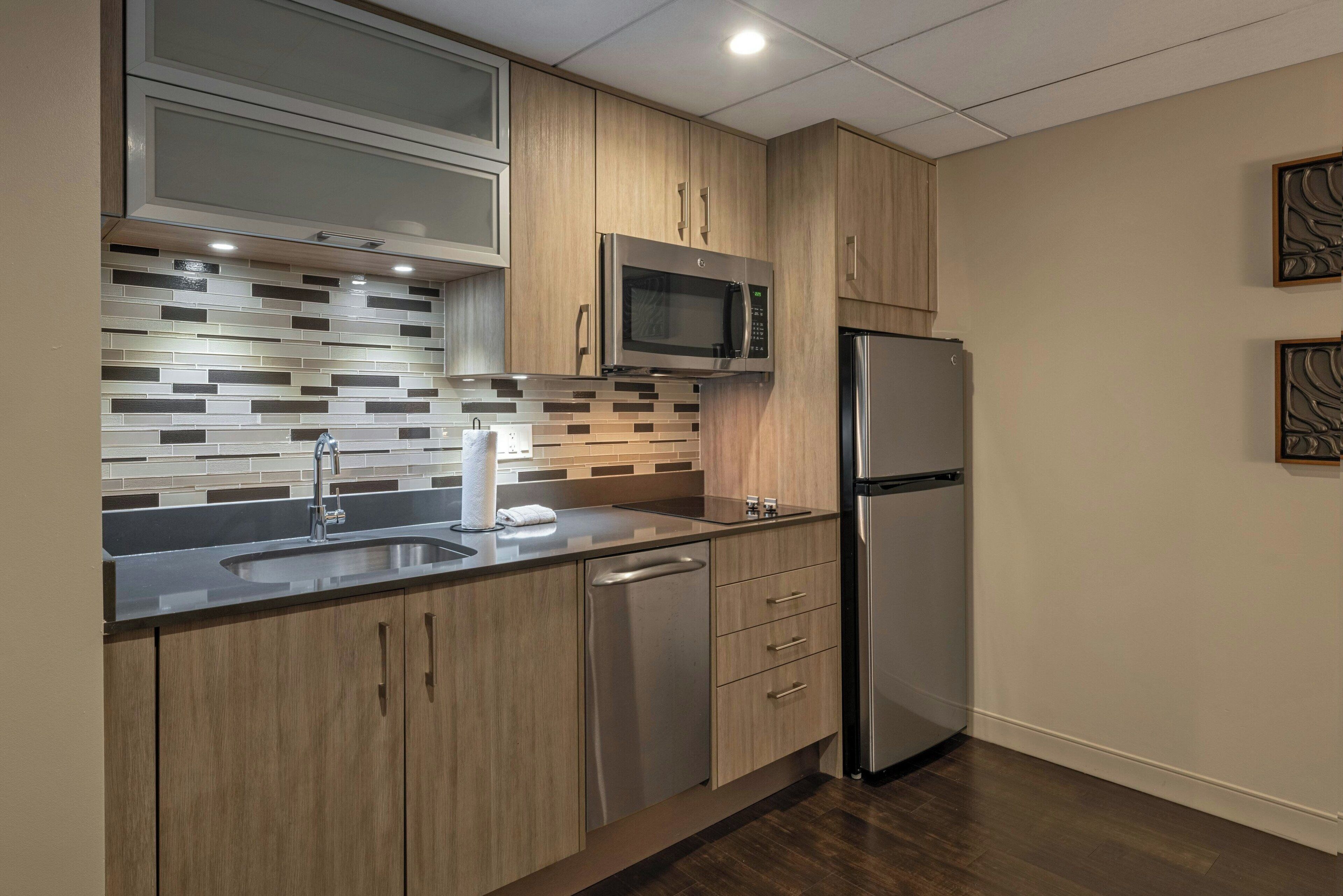 A modern kitchen with wooden cabinets, a stainless steel refrigerator, a microwave, and a tiled backsplash.
