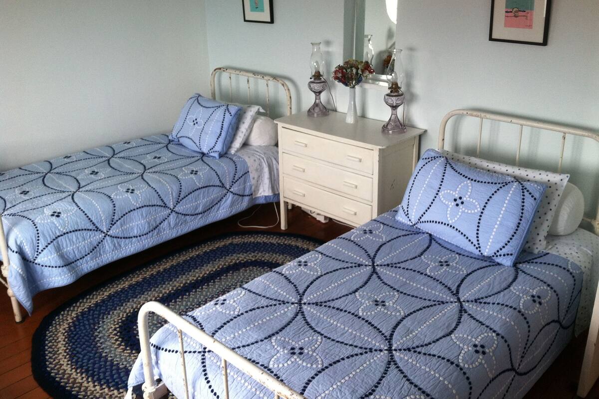 A bedroom with two single beds, a bedside table with a mirror, and a dresser.