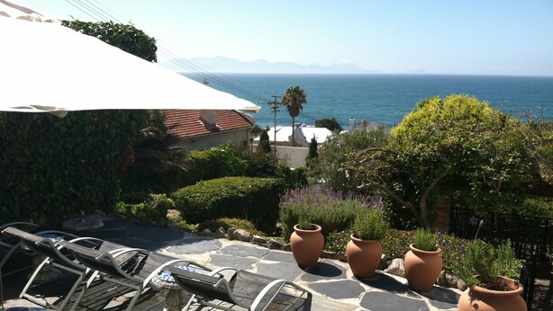 A patio with outdoor furniture, potted plants, and a view of the sea. - Blue On Blue Bed and Breakfast (Cape Town)