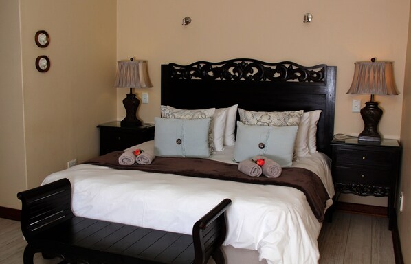 A neatly made bed with a dark headboard, two bedside tables with lamps, and a small wooden bench at the foot of the bed.