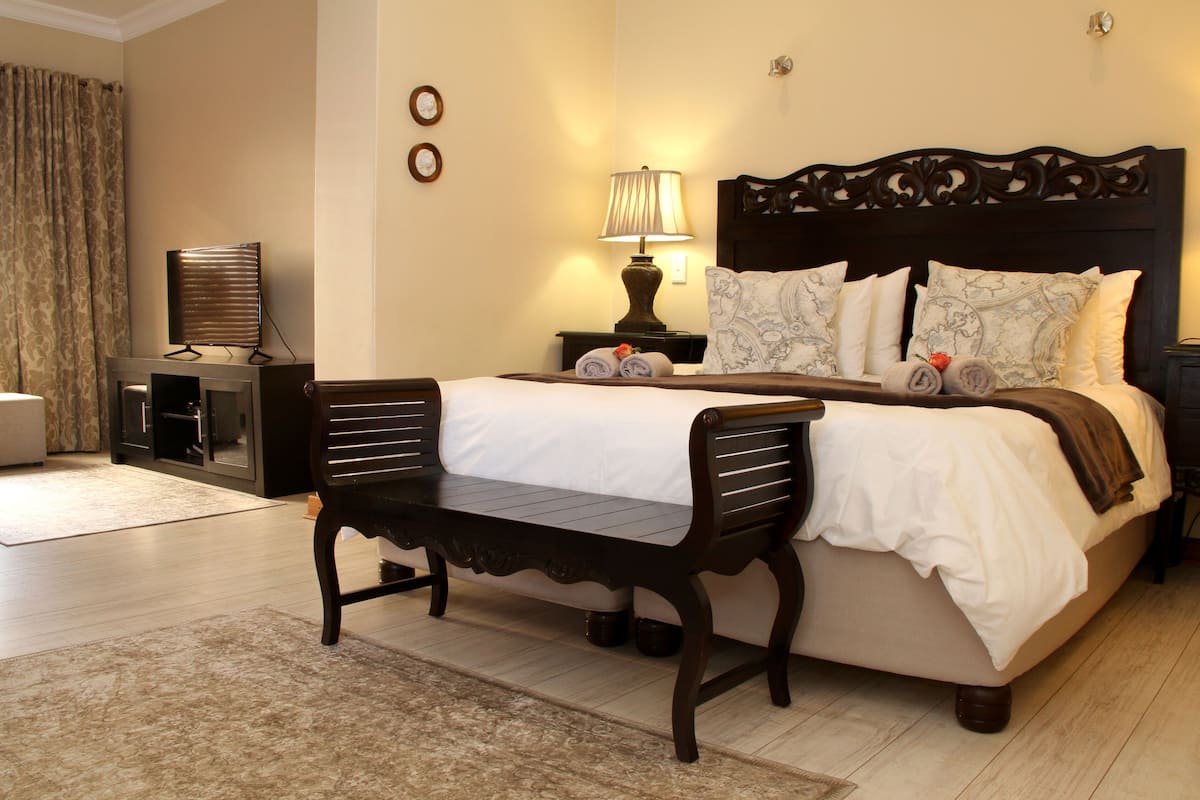 A hotel room with a large bed, a bedside table with a lamp, a small desk with a computer, and a chair.