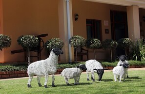 Fachada de edificio con una serie de esculturas decorativas de ovejas en el césped.