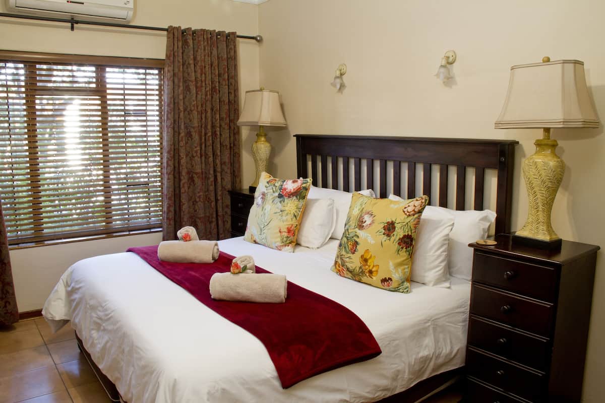 A neatly made bed with floral pillows, a red throw blanket, and two bedside lamps.